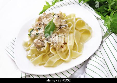 Tagliatelle pasta with salmon, cream, garlic and herbs in a plate on a kitchen towel, fork, parsley and basil on white wooden board background Stock Photo