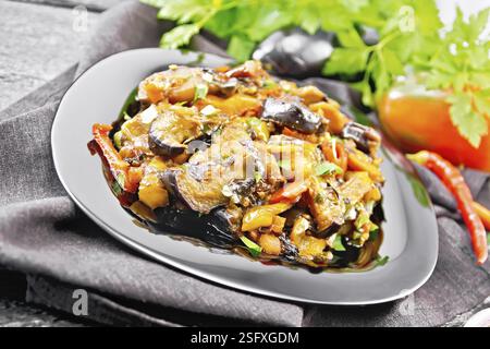 Vegetable ragout with eggplant, tomatoes, sweet and hot peppers, onions, carrots, fried with herbs and spices in a plate on a towel, garlic, parsley o Stock Photo