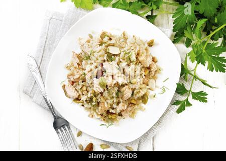 Salad of smoked salmon, rice, sunflower and pumpkin seeds, almonds, seasoned with honey and olive oil in a plate on a towel, parsley and fork on woode Stock Photo