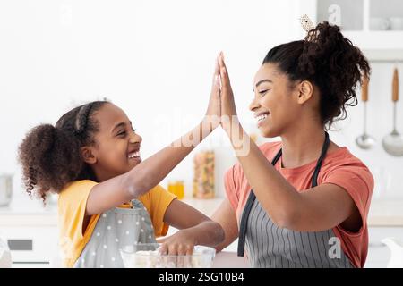 Cheerful black mother and daughter giving high five while cooking Stock Photo
