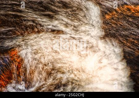Abstract long-exposure image of rushing water over rocks, creating a dynamic textured pattern. Stock Photo