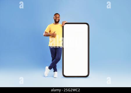 Handsome African American guy standing near big cellphone with empty screen, showing thumb up Stock Photo