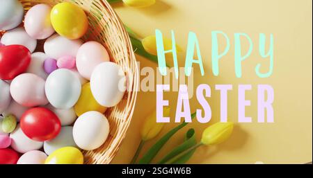 Image of happy easter text over colourful eggs in basket on yellow background Stock Photo
