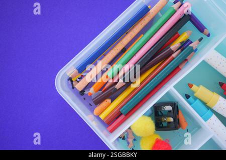 Colorful art supplies in a clear container on a purple surface Stock Photo