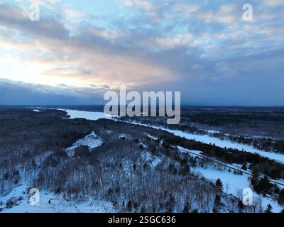 A vast, snow-covered forest landscape with a road cutting through the center is seen from above under the deep blue and pink clouds of twilight Stock Photo