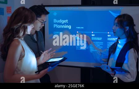 asian leader present  business presentation in a dimly lit office, analyzing financial charts and data projections on a screen Stock Photo
