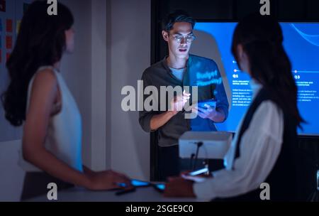 asian leader present  business presentation in a dimly lit office, analyzing financial charts and data projections on a screen Stock Photo