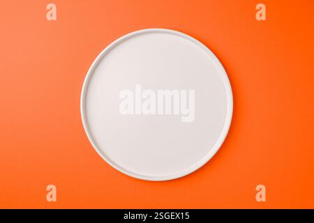 Top view of empty ceramic white plate on orange background Stock Photo