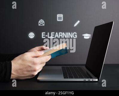 Hands holding open book next to laptop with e-learning icons, representing online education and learning opportunities Stock Photo