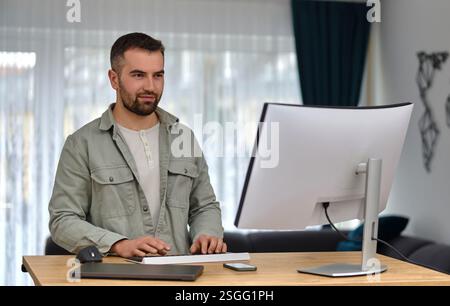 A happy man using a desktop computer while working at a home. Stock Photo