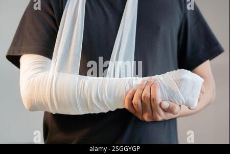 Close-up of man with bandaged hand and arm support standing over light gray color background. Emergency concept. Stock Photo