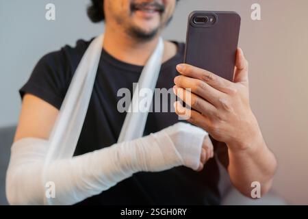 Happy middle aged man wearing a black shirt with hand injury uses smartphone. Medical and healthcare concept Stock Photo