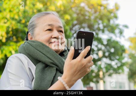 Portrait image of happy senior Asian woman looking at smart phone, using mobile phone at outdoor. Stock Photo