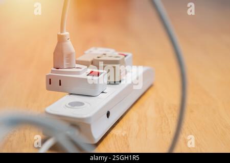 An electric plugged into maltiple electrical outlet on wooden table. Concept of electricity consumption. Selective focus. Stock Photo