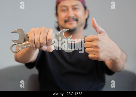 Cropped image of mechanics working in auto service. One is holding a wrench and showing Ok sign. Selecitve focus. Stock Photo