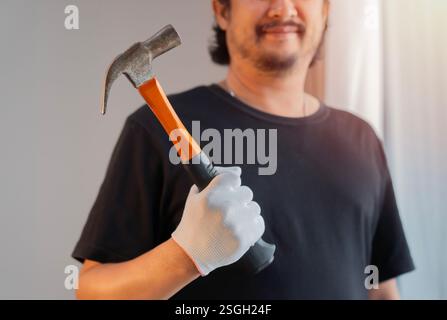 Cropped shot of handsome Asian man in black t-shirt holding hammer at home. Selective focus. Stock Photo
