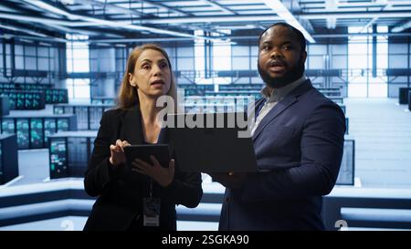 Manager in data center supervising worker running error checking utilities to fix errors. Supervisor in server farm overseeing engineer repairing network issues affecting rigs performance, camera A Stock Photo