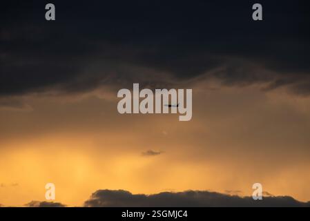 A lone aircraft glides through a cloudy sunset sky, silhouetted against vibrant hues of orange and deep gray. The atmosphere evokes a sense of adventu Stock Photo