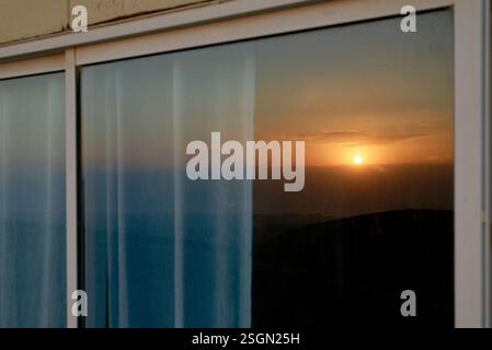 Sunset reflected on a hotel room window with curtains softly illuminated by the evening light. Israel Stock Photo