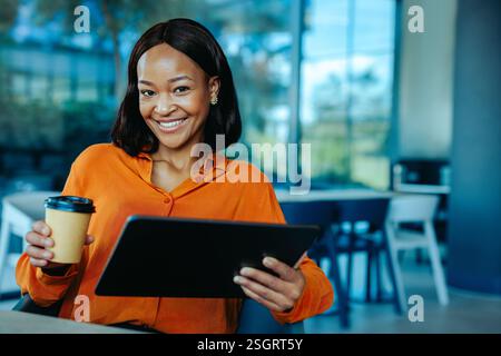 A confident African accountant in a bright orange blouse is seated in a modern office environment. The setting exudes productivity and collaboration, Stock Photo
