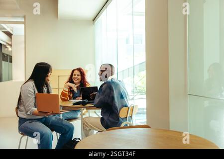 A group of college friends studying together with laptops and books in a stylish, bright environment. They are engaged in collaborative study and idea Stock Photo