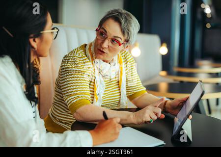 Mature woman provides a private teaching lesson to a young student, using a tablet for an interactive learning experience in a modern setting with foc Stock Photo