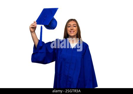 Young woman smiling while wearing a blue graduation gown and holding her graduation cap, joyfully celebrating her college graduation against a clean w Stock Photo