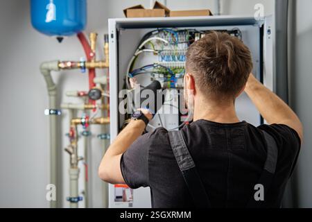 Technician working on internal wiring of heat pump, inspecting electrical connections. Specialist servicing heating and cooling system. Electrician wi Stock Photo