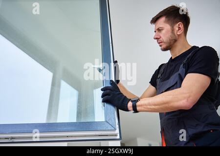 Professional repairman adjusting white pvc windows in modern building. Construction worker installing plastic window in new home. Concept of repair an Stock Photo