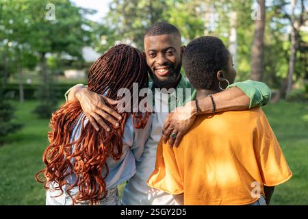 Cunning African American man hugs two women with backs to camera