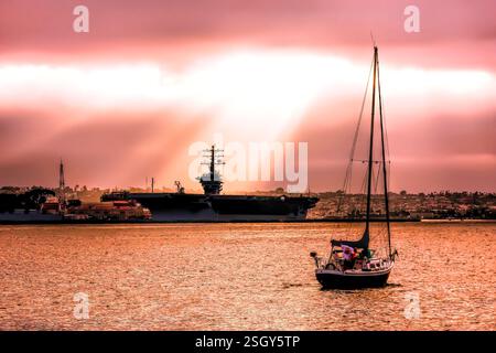 Small sailboat is sailing in the ocean next to a large Navy ship. The sun is shining on the water, creating a beautiful and peaceful scene Stock Photo