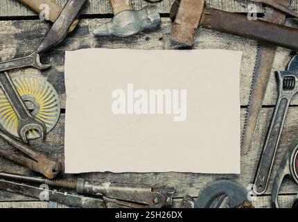 Various hand tools arranged around a blank sheet of paper on a wooden table ready for a project Stock Photo