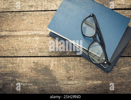 Stack of blue notebooks and glasses resting on a rustic wooden table during a sunny afternoon Stock Photo