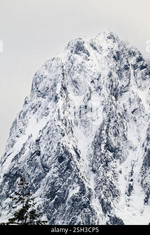 Rugged snow covered peak of mount index rising in winter against gray sky Stock Photo