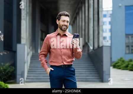 Confident Businessman Using Smartphone While Standing Outside an Office Building. Stock Photo
