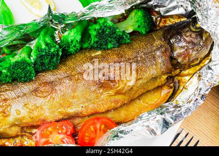 Freshly cooked trout served with steamed broccoli, cherry tomatoes, and lemon in foil wrap for a healthy meal Stock Photo
