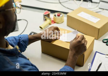 Hands of young male worker of warehouse putting sticker with barcode on top of packed box with newly produced equipment Stock Photo