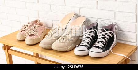 Stylish shoes and orthopedic insoles on wooden rack near light brick wall Stock Photo
