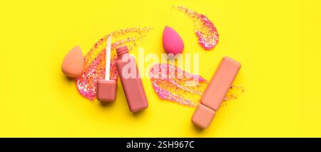 Pink lipsticks with makeup sponges and glitter on yellow background Stock Photo