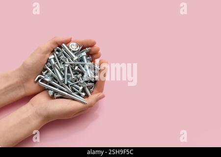 Female hands holding pile of different tap bolts and screws on pink background Stock Photo