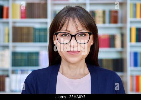 Headshot portrait of friendly mature woman in glasses inside library office Stock Photo