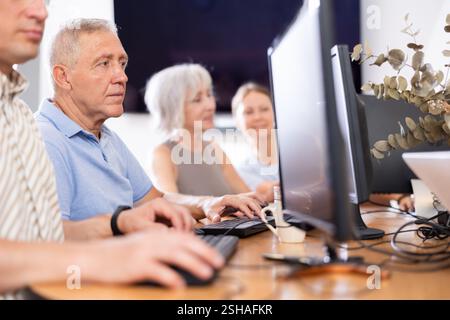 Concentrated elderly man immersed in using computer in library Stock Photo