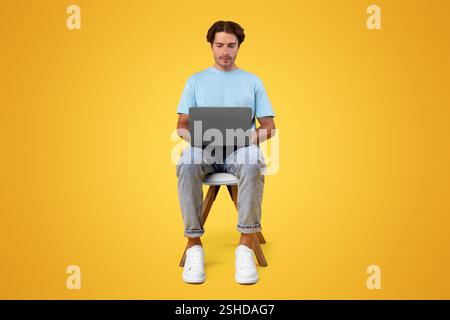 Serious guy using laptop sitting on chair at studio Stock Photo