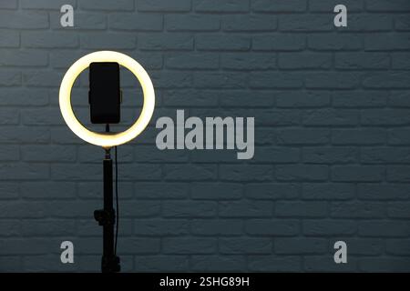 Ring lamp with smartphone against brick wall, space for text Stock Photo
