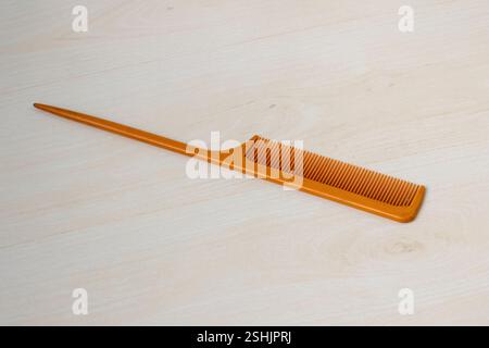 An orange plastic hair comb rests on the light wooden surface. Stock Photo