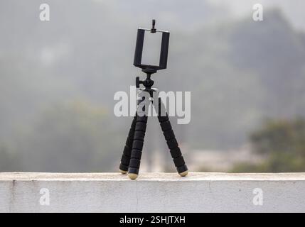 Black Flexible mini octopus tripod with Bracket Holder Mount, placed on an outdoor wall with a blurred background. Compatible with smartphones and cam Stock Photo