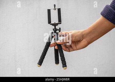 A female hand holds a black, flexible mini octopus tripod with a bracket holder mount, shown against a white background. Compatible with smartphones a Stock Photo