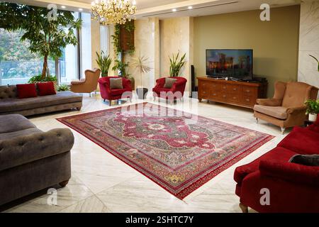 Luxurious living room with a traditional Persian rug, tufted grey sofa, red armchairs, and marble flooring. Stock Photo
