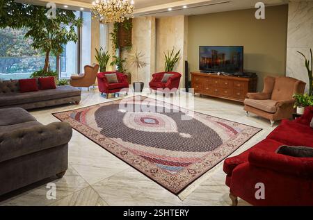 Stylish living room featuring a dark-centered Persian rug with oval medallions, marble flooring, and comfortable seating. Stock Photo