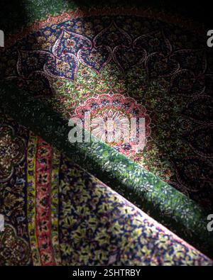 Overlapping folds of a richly patterned Persian rug featuring a central medallion and floral motifs in dark jewel tones Stock Photo